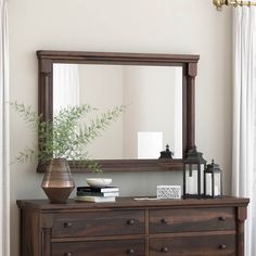 a wooden dresser topped with a mirror next to a plant and vase on top of it