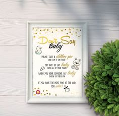 a framed poster with the words don't say baby on it next to a potted plant