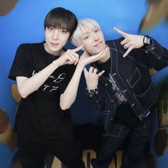 two young men standing next to each other in front of a blue wall with gold letters