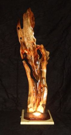 a wooden sculpture sitting on top of a white base next to a black background with the image of a tree trunk carved into it