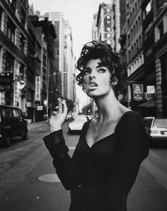 a woman standing on the side of a road next to tall buildings