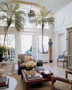 a living room filled with lots of furniture and palm trees in the window sill