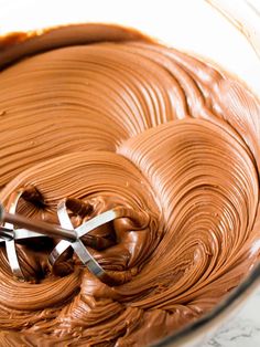 a mixing bowl filled with chocolate frosting and a whisk in the middle