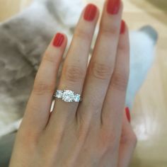 a woman's hand with a three stone ring on her finger and red nail polish