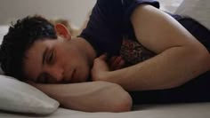 a man laying in bed with his head on the pillow and looking at the camera