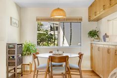 a dining room table and chairs in front of a window with potted plants on it