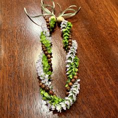 two necklaces made out of flowers and beads on a wooden table with a bow