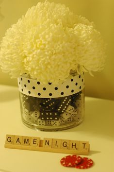 a vase filled with white flowers next to a scrabble letter and game pieces