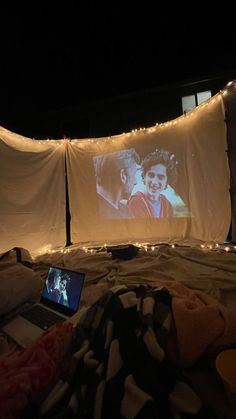 a laptop computer sitting on top of a bed covered in blankets and fairy lights,