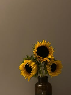 a vase filled with yellow sunflowers on top of a wooden table next to a wall