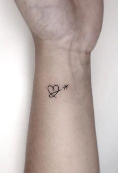 a small heart and an arrow tattoo on the left side of the wrist is shown