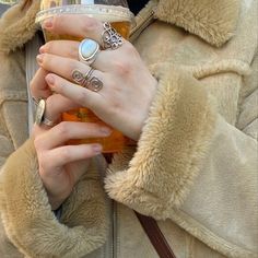 a woman in a fur coat holding a drink and wearing rings on her fingers,