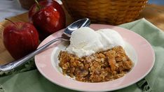 an apple crisp with ice cream on a pink plate next to two baskets of apples