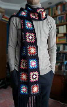 a man wearing a scarf with crocheted flowers on it in front of a bookshelf