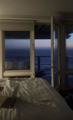 a laptop computer sitting on top of a bed next to two large windows overlooking the ocean