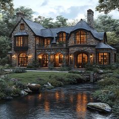 a large stone house sitting next to a river in front of a lush green forest