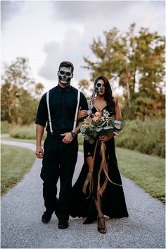 a man and woman in skeleton makeup walk down a path together, dressed in black