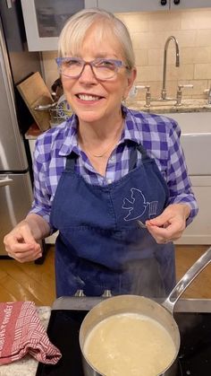 an older woman wearing glasses is stirring something in a pot on the stove top with a ladle