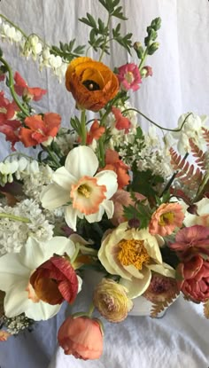 a vase filled with lots of different colored flowers on top of a white table cloth