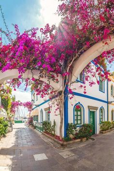 a white and blue house with pink flowers on it's roof next to the ocean