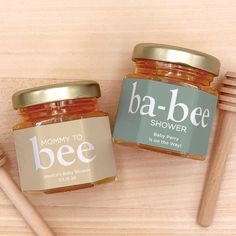 two jars of baby bee honey sitting on top of a table next to a wooden spoon