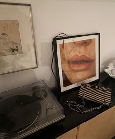 an old record player is sitting on top of a dresser next to a framed photograph of a woman's face