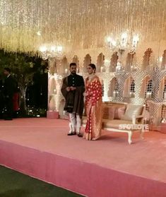 a man and woman standing on a stage in front of chandelier hanging from the ceiling