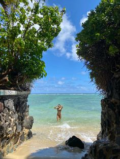 a person standing in the water near some rocks and trees with their arms out to the side