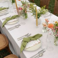 a long table set with place settings and flowers in vases on the tablescloth