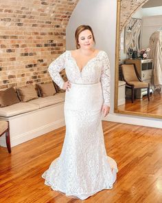 a woman standing in front of a mirror wearing a white wedding dress with long sleeves