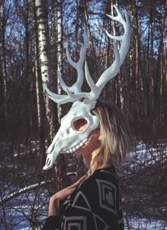 a woman wearing a deer head mask in the woods with snow on the ground and trees behind her