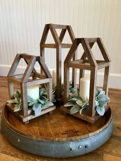 three small wooden houses with candles in them on top of a wood tray, surrounded by greenery