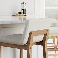 a white counter top sitting under a window next to a wooden bar stool with a gray seat