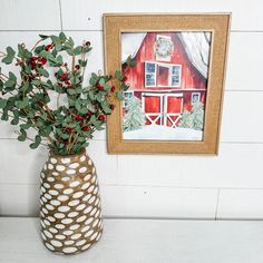 a vase filled with red berries and greenery next to a framed painting on the wall