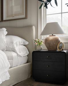 a bed with white sheets and pillows next to a nightstand with a lamp on it