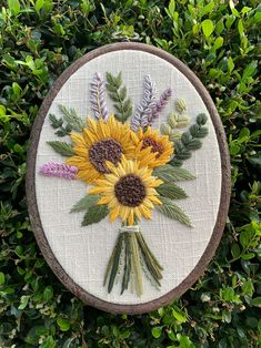 a cross - stitch sunflower and other flowers in a wooden frame on some bushes