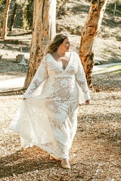 a woman in a white dress walking through the woods