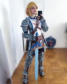 a woman dressed in armor holding a cell phone and standing on a hard wood floor