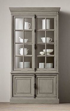 a gray china cabinet with glass doors and dishes on it's sides, in front of a white wall