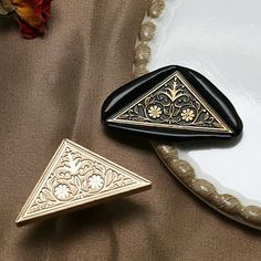 two black and gold trinkets sitting on top of a white plate next to a flower