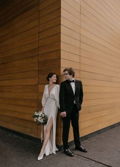 a man and woman standing next to each other in front of a wall with wooden panels