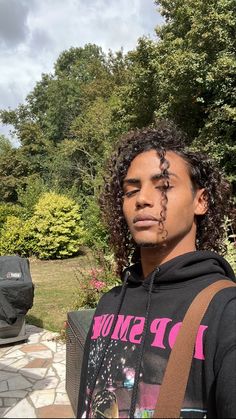 a young man with long curly hair wearing a black sweatshirt and carrying a brown bag