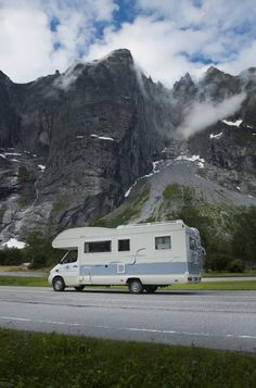 an rv is parked on the side of the road in front of mountains and clouds