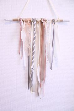 a white wall hanging with ribbons and laces attached to it's sides on a wooden stick