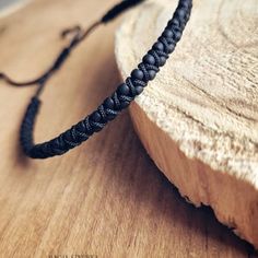 a black braided bracelet sitting on top of a wooden table next to a piece of wood