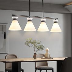 a dining room table with four lights hanging over it and a vase on the table