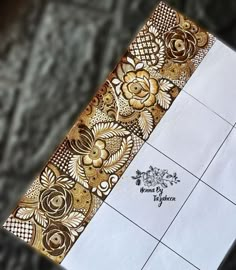 an intricately designed piece of paper on top of a tile floor with gold and white designs