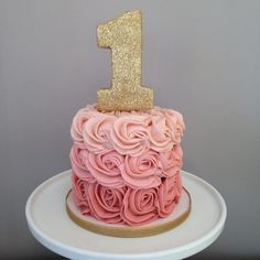 a pink and gold birthday cake on a white plate with a number one topper