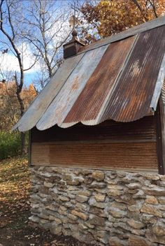 an old building made out of wood and stone with a metal roof in the woods