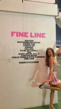 a woman standing next to a white wall in front of a sign that says fine line